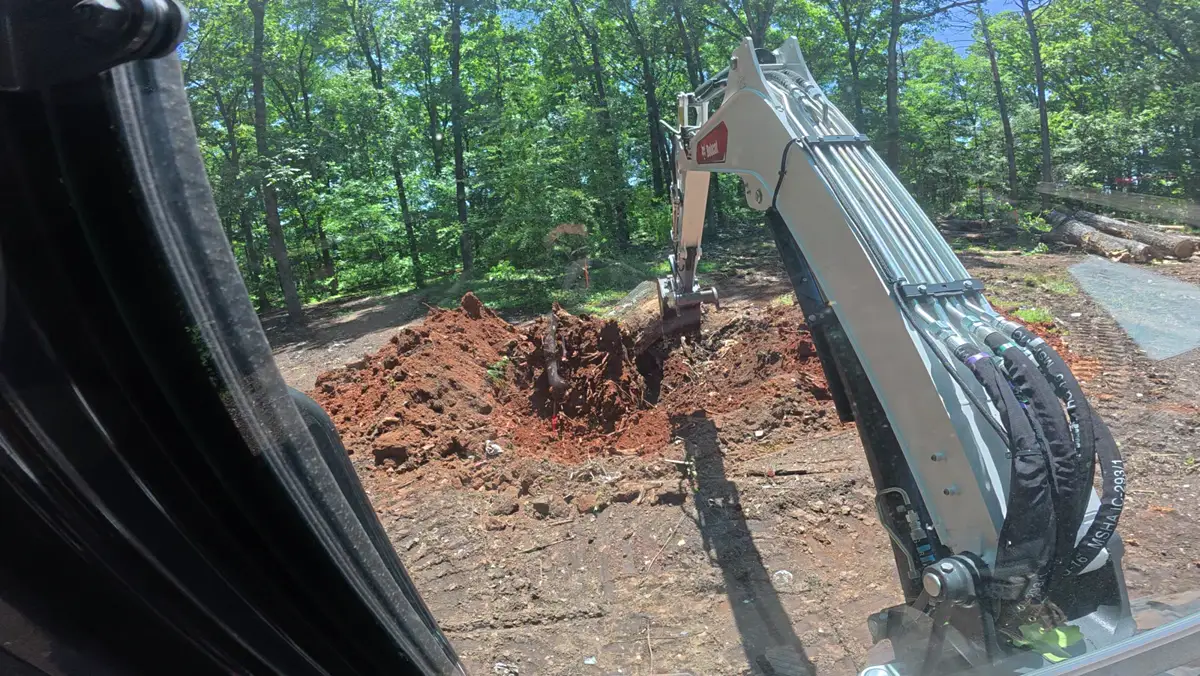 Excavator digging a stump out of red dirt
